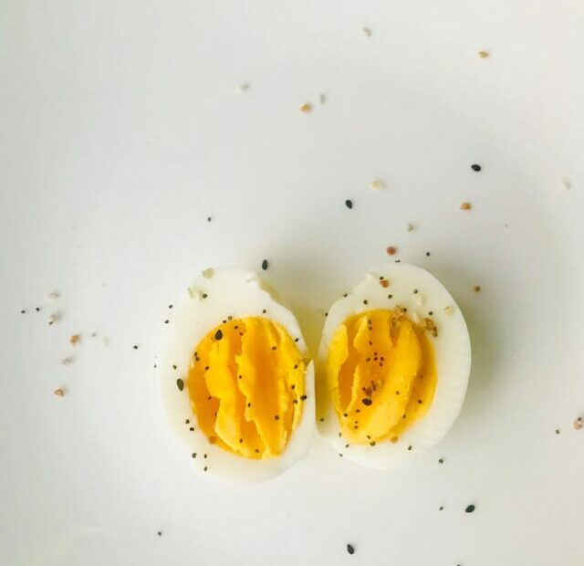 A close-up of a sliced boiled egg with pepper seasoning on a white plate, ideal for healthy meals.
